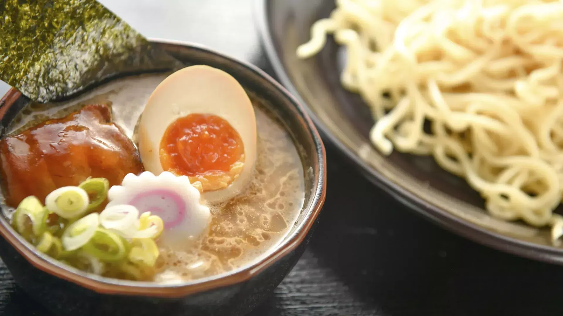 Immagine ravvicinata di una ciotola di noodles e una ciotola di zuppa di ramen con un uovo in camicia, 切成两半.