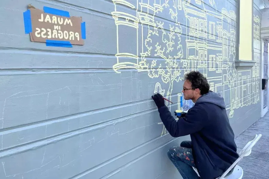 一名艺术家在Mission District一幢建筑物的一侧画壁画, con un letrero pegado en el edificio que dice "Mural en progreso". San Francisco, CA.