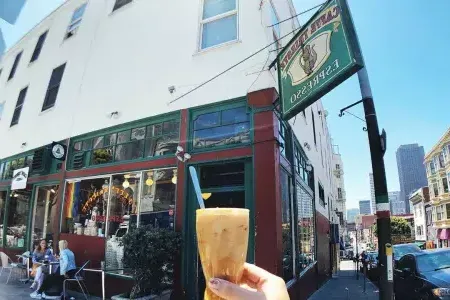 A person's h和 holds a coffee drink with the exterior sign 和 storefront of 咖啡的里雅斯特 in the background.