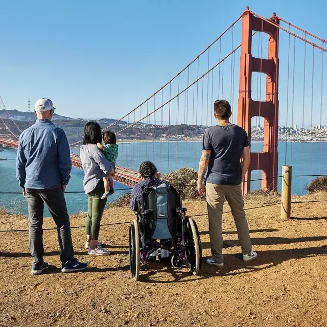 一群人, 包括一个坐轮椅的人, è visto da dietro mentre guarda il 金门大桥 da Marin Headlands.