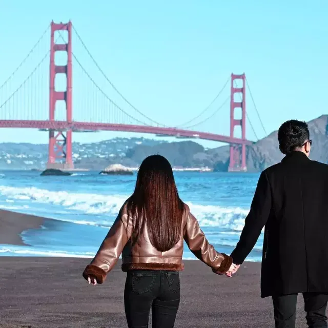 Pareja tomados de la mano en Baker Beach con el 金门大桥 en segundo plano 