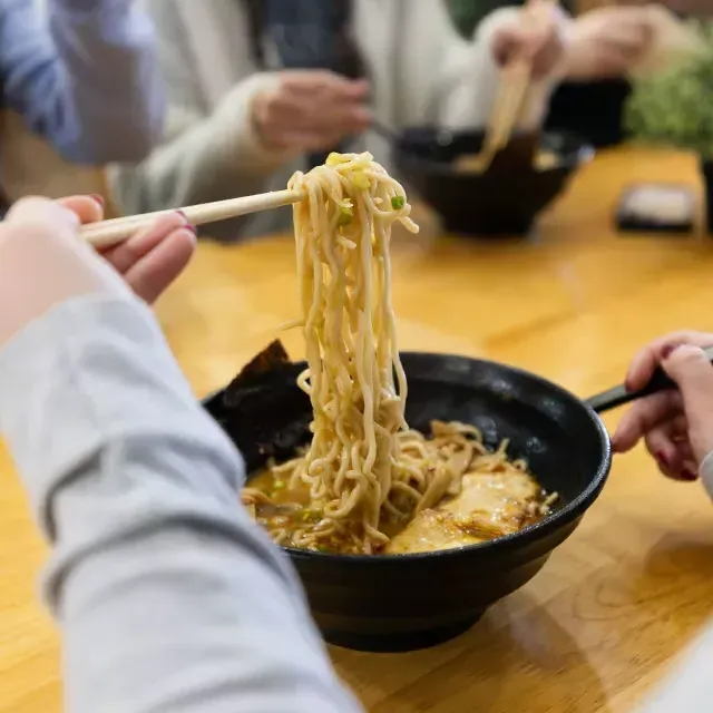 Person lifting ramen noodles out of a bowl with chopsticks